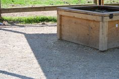 a wooden box sitting on top of a dirt ground next to a fence and grass field