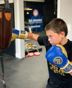 a young boy wearing blue and yellow boxing gloves with his hand on a punching bag