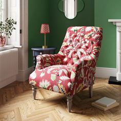 a red chair sitting in front of a green wall next to a lamp on a wooden floor