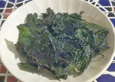 a white bowl filled with lettuce on top of a blue and red tile floor