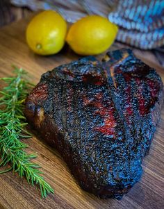 a piece of steak sitting on top of a wooden cutting board next to lemons