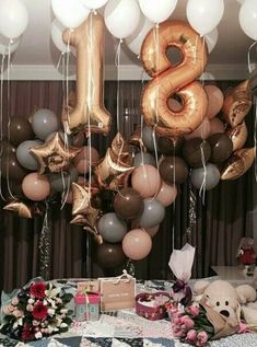 a table topped with balloons and stuffed animals in front of a number eight balloon wall