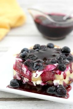 a dessert with blueberries and cream on a white plate next to a bowl of fruit