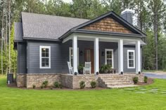 a small gray house with white trim and columns on the front porch is surrounded by trees