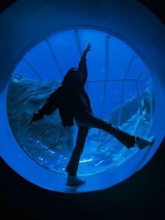 a person standing in front of an aquarium looking at the water and holding their arms up