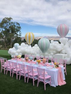 a table set up for a party with hot air balloons in the sky above it