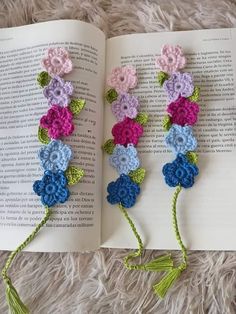 an open book with crocheted flowers on it and tassels attached to the pages