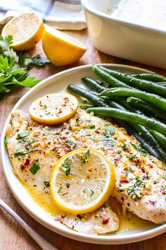 a white plate topped with chicken, lemons and asparagus next to green beans