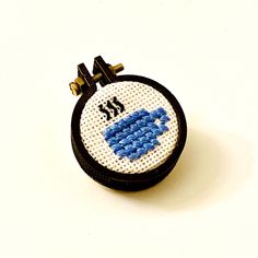 a small blue and white cross stitched object on a white surface with black trim