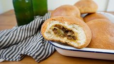 some bread rolls sitting in a white bowl on a table next to a green bottle