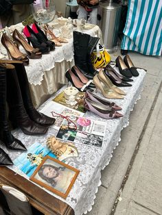 several pairs of shoes are on display at an outdoor market table with pictures and other items