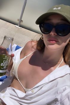 a woman in sunglasses and a hat is holding a glass with some liquid on it