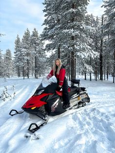 a woman sitting on top of a snowmobile in the middle of a snowy forest