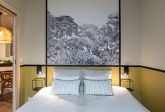 a bed with white sheets and pillows in a bedroom next to a painting on the wall