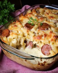 a casserole dish with sausage and pasta in it on a pink cloth next to a green plant