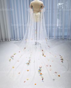 a wedding dress on display in front of a window with sheer drapes and flowers