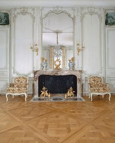 an ornate fireplace in the middle of a room with white walls and gold trimmings