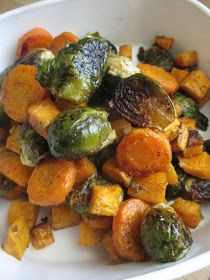 a white bowl filled with roasted vegetables on top of a wooden table next to a fork