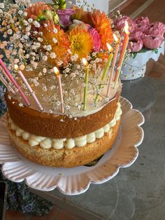 a cake with candles and flowers on it is sitting on a plate in front of other cakes