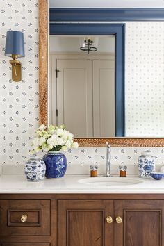 a blue and white vase with flowers in it sitting on a bathroom vanity next to a mirror