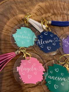 four personalized acrylic keychains with tassels on a tree slice