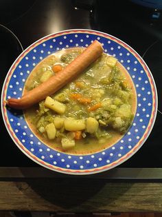 a blue and white plate topped with soup and a hot dog on top of it