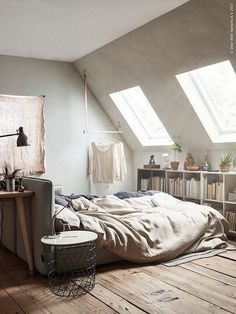 a bed sitting under two windows in a bedroom next to a book shelf and lamp