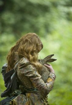 a woman with long red hair wearing a leather jacket and carrying a bird on her back