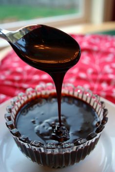 spoon drizzling melted chocolate onto a cupcake liner on a white plate