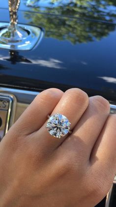 a person's hand with a diamond ring on their finger next to a car