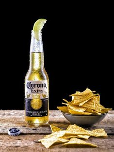 a bottle of corona beer next to chips on a wooden table with a black background