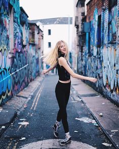 a woman is dancing in an alleyway with graffiti on the walls and buildings behind her