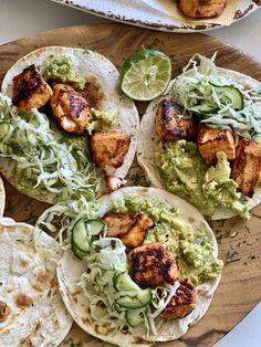 three tacos with chicken, guacamole and lime wedges on the side