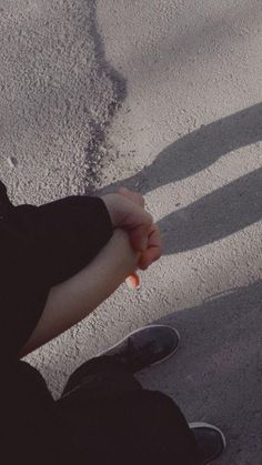 a person sitting on the ground holding an orange object in one hand and their shadow behind them