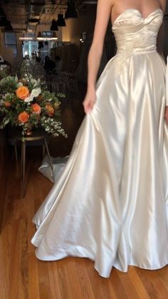 a woman in a white wedding dress standing on a hard wood floor next to a vase with flowers