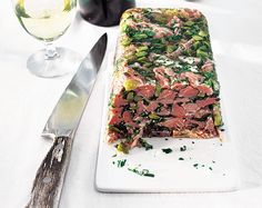 a white plate topped with meat and veggies next to a glass of wine