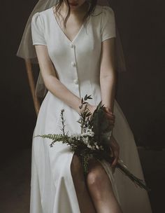 a woman sitting on a chair with a bouquet in her hand and wearing a wedding dress