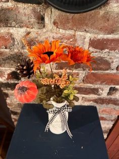 an arrangement of flowers in a white vase on a blue table next to a brick wall