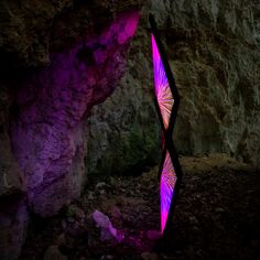 a purple light is shining on the rocks in front of a large rock formation that looks like an abstract piece of art