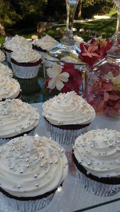 several cupcakes with white frosting are on a glass table next to some wine glasses