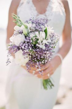 a woman holding a bouquet of flowers in her hands and wearing a white wedding dress