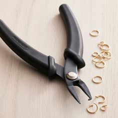 a pair of pliers sitting on top of a wooden table next to gold rings