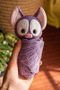 a hand holding a purple knitted toy with eyes