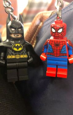 two lego batman and spider man keychains sitting on top of each other's purse