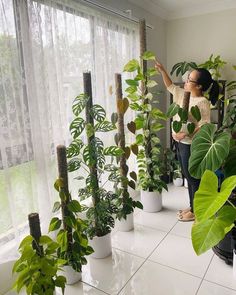 a woman standing in front of a window next to lots of potted plants and trees