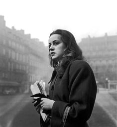 black and white photograph of a woman standing in front of an old street with buildings