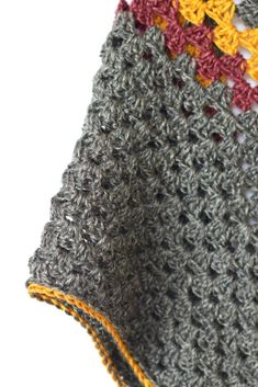 a crocheted blanket with yellow and red trims sitting on top of a white surface