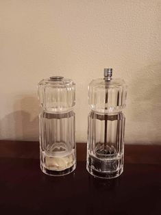 two clear glass salt and pepper shakers sitting on a wooden table next to a wall