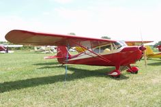 a small red airplane sitting on top of a lush green field next to other planes