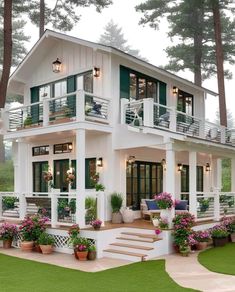 a white house with green shutters and flowers on the front porch is surrounded by greenery